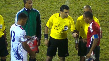 Photo: Belizean referee Irfan Basdemir (centre) gives it a toss while Trinidad and Tobago captain Densill Theobald (far right) and Belize captain Dalton Eiley (far left) look on. (Courtesy TTFF Media)